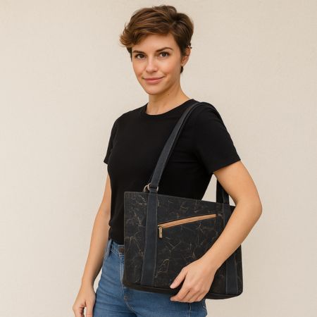 Woman holding a black cork leather shoulder bag against a plain background