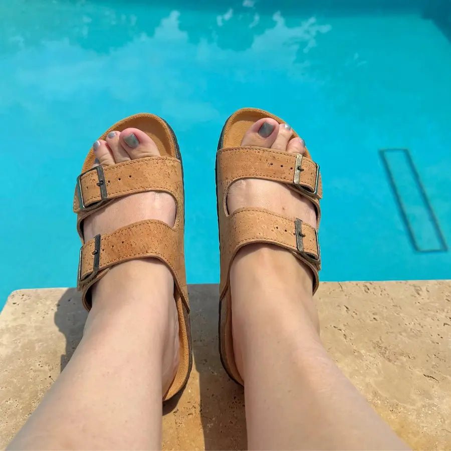 Brown two-strap sandals worn by a person sitting by a pool.