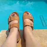 Brown two-strap sandals worn by a person sitting by a pool.