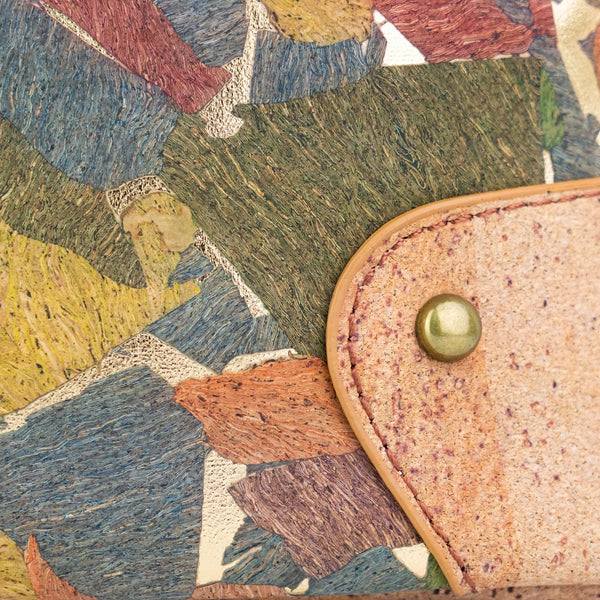 Close-up detail of the Arlington cork bag  a multicolor abstract patterned background and a tan leather tab secured by a brass rivet.