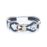 A multi-strand wrap bracelet featuring navy blue and tan cork cords, silver-tone floral charms, and a silver-tone magnetic clasp, shown on a plain white background.