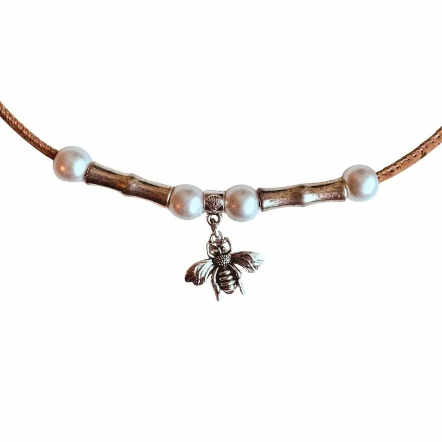 Close up of cork necklace with pearl beads and a bee charm on a white background