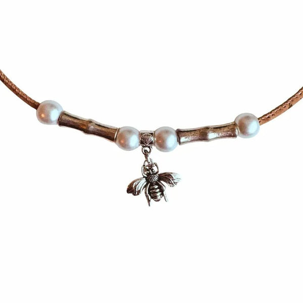 Close up of cork necklace with pearl beads and a bee charm on a white background