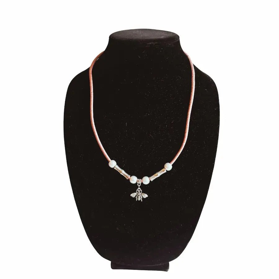 Necklace of pink cork cord with a bee charm on a black velvet stand against a white background