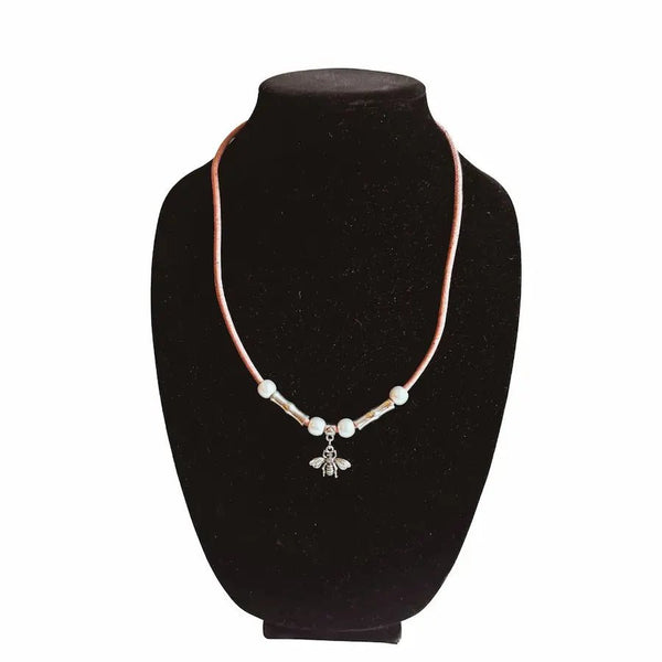 Necklace of pink cork cord with a bee charm on a black velvet stand against a white background
