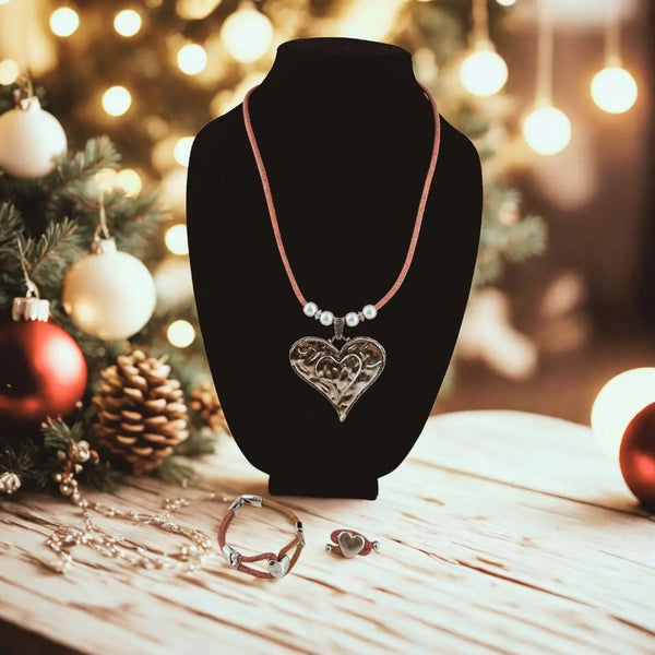 Necklace with a heart pendant with bracelet and ring with heart charms  on a black stand against a festive background with Christmas decorations.