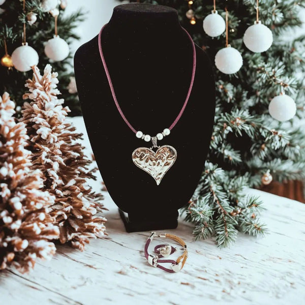 Necklace with a heart pendant with bracelet and ring with heart charms  on a black stand against a festive background with Christmas decorations.
