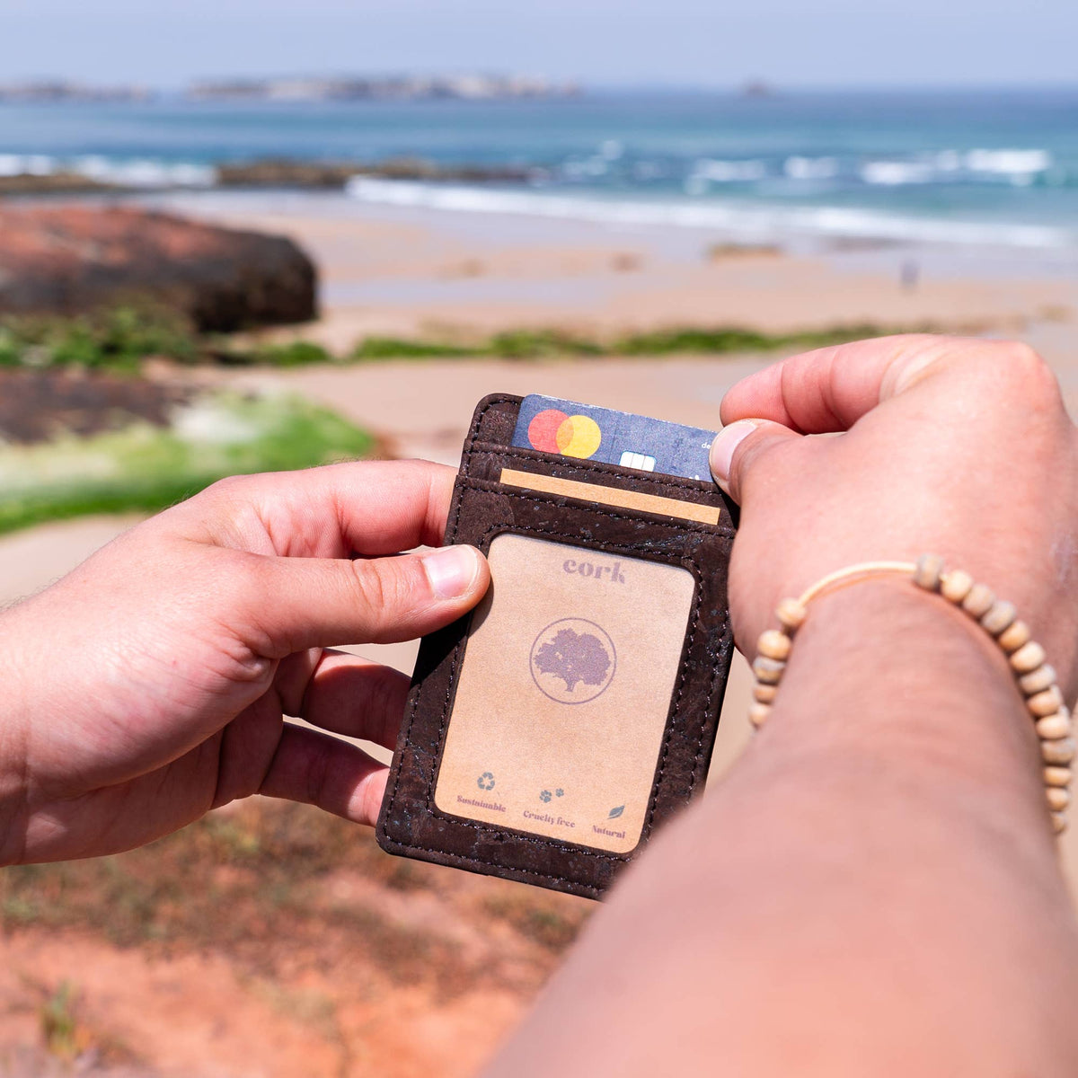 Person holding a cork leather minimalist card wallet with cards on a beach