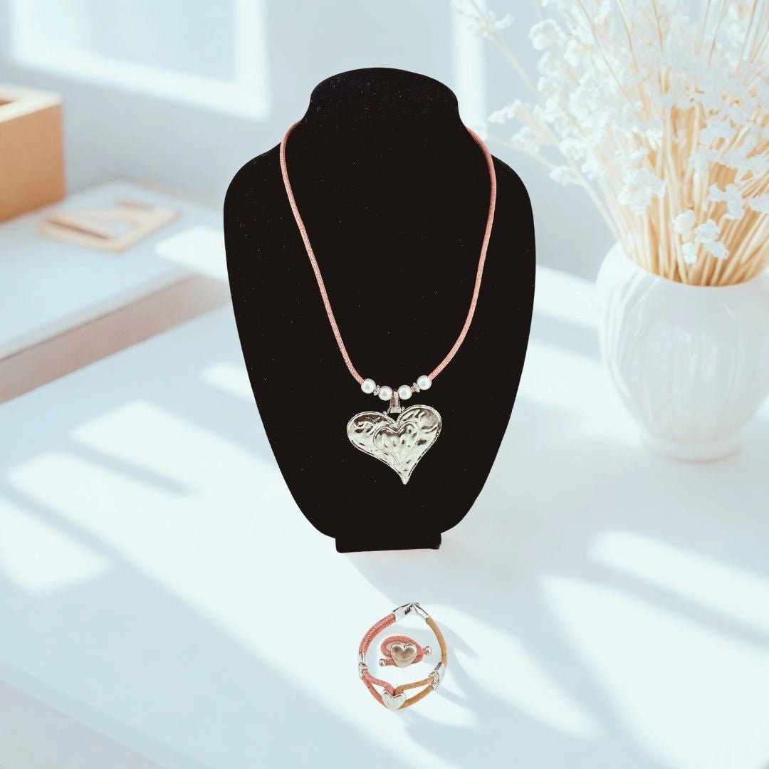 Necklace with a heart pendant on pink cork cord with bracelet and ring with heart charms  on a black stand.