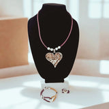Necklace with a heart pendant on purple cork cord with bracelet and ring with heart charms  on a black stand.
