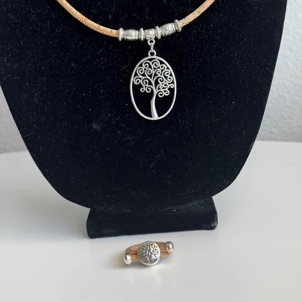 Necklace with tree pendant on a black stand and ring with tree imprint on table